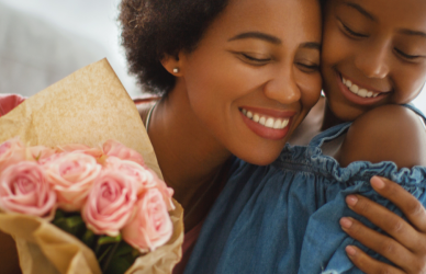 black mother and daughter hugging with bouquet of flowers