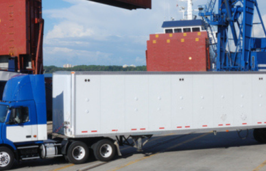 semi truck at port with cargo ship and crane in background