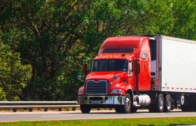 red semi truck pulling white trailer on road with trees in background