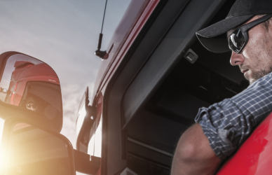 Man wearing hat and sunglasses in cab of red semi truck