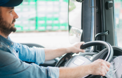 man sitting in cab of semi truck with hands on steering wheel