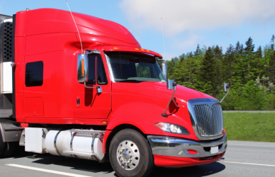 red semi truck with white trailer parked on side of road with trees in background