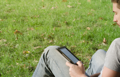 man leaning against tree reading ebook