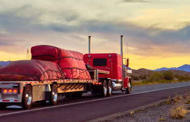 red flatbed truck with red cargo cover driving into sunset with mountains in the background