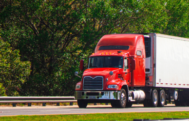 red semi truck pulling a white trailer on road with trees in the background