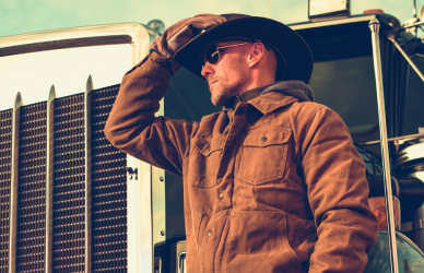 man in work jacket and cowboy hat standing in front of semi truck