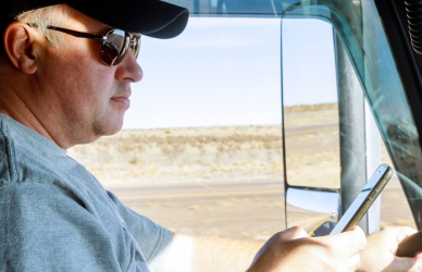 Man sitting in semi truck cab looking at smartphone