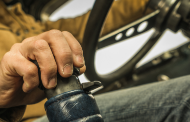 truck driver in cab with one hand on steering wheel and one hand on gear shift