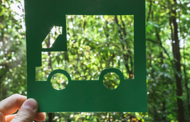 hand holding up cutout of truck in front of a forest of trees