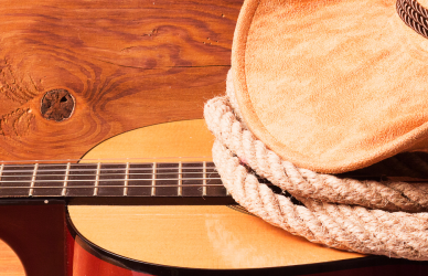 acoustic guitar, cowboy hat, and rope on wood background