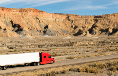 red semi truck pulling white trailer across a desert landscape