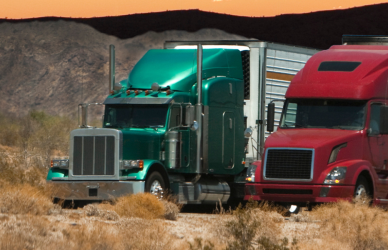 red and green semi trucks with white trailers and mountains in background