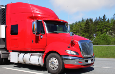 red semi truck pulling white trailer on road with green grass and trees in background
