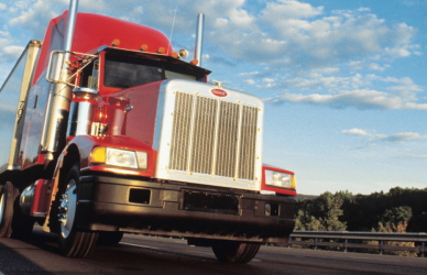 red semi truck on road trees in background and a blue sky with a few clouds