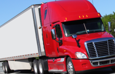 red semi truck with white trailer driving on road with bridge and trees in background