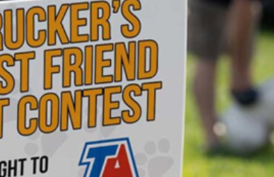 grassy area with sign the reads "trucker's best friend pet contest" and a man with a white dog in the background