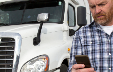 Man in flannel shirt looking at cell phone with white semi truck in background
