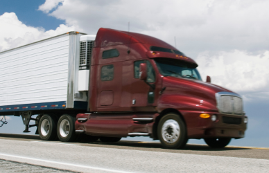 dark red semi truck with white trailer parked on road with partly cloudy sky in background