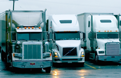 variety of semi trucks parked in a row in a parking lot on a rainy day