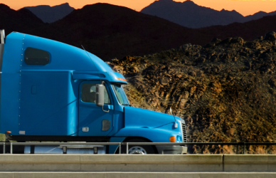 blue semi truck with white trailer on road with mountains and sunset in background