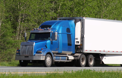 blue semi truck pulling white trailer on road with trees in background