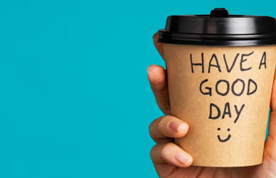disposable coffee cup that reads "have a great day" being held up on blue background driver appreciation week