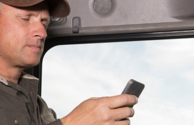 man in cab of semi truck at steering wheel looking at phone, truck parking, truck parking app, trucklots