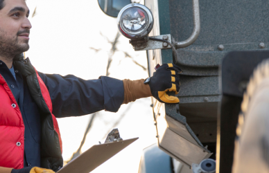 man in red vest holding clipboard standing next to semi truck, truck inspections, roadcheck