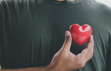 man in gray t-shirt holding red heart up over chest