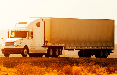 semi truck in the glow of sunset parked on pavement with mountains in the back ground