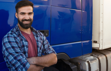 Semi truck driver leaning on semi truck with folded arms