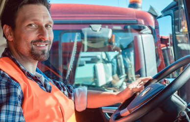 man wearing orange safety vest in cab of semi truck at steering wheel