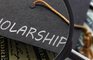 graduation cap with the word scholarship printed on it under a magnifying glass with money bills in the background