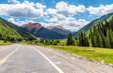 highway in colorado with blue sky and fluffy clouds and mountains