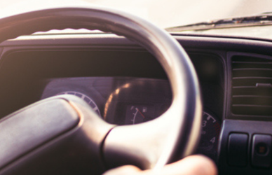 Truck driver in semi truck cab with hands on steering wheel looking out over road through windshield