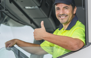 man in bright yellow shirt sitting in cab of white semi truck with window rolled down at the steering wheel giving a thumbs up