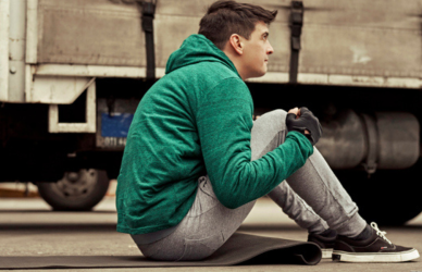 man in green hoodie and sweatpants with yoga mat next to semi truck