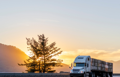 semi truck on highway with mountains, trees, and sunset in background