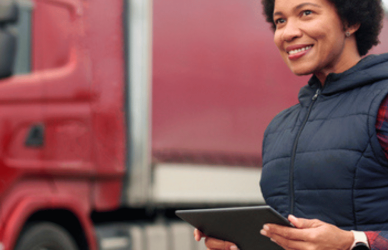 woman holding tablet in front of semi trucks