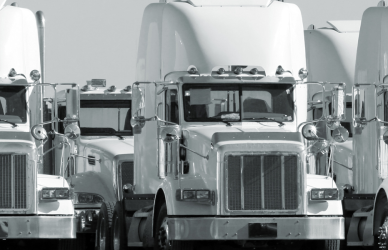 black and white photo of several semi trucks that are mostly the same make and model parked together in a group or fleet