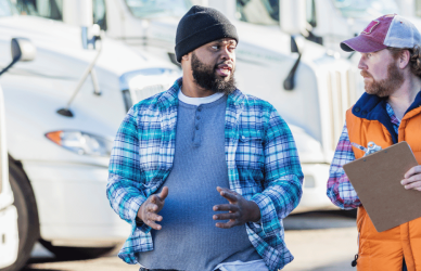 two men talking in front of semi trucks