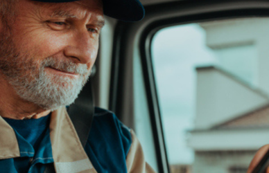 older trucker looking at phone in cab