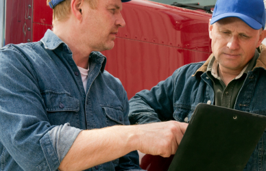 two men looking at clipboard with semi truck in background