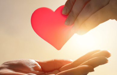 Hand giving heart to a receiving hand