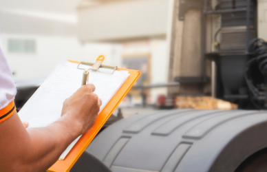 man in safety vest with clipboard standing near semi truck