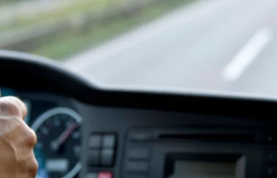 man at the wheel of a semi truck looking out of the cab at the road ahead