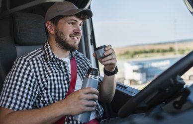 Positive truck driver drink coffee in his cabin.