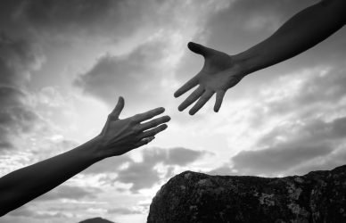 Hand helping another up a mountain path.